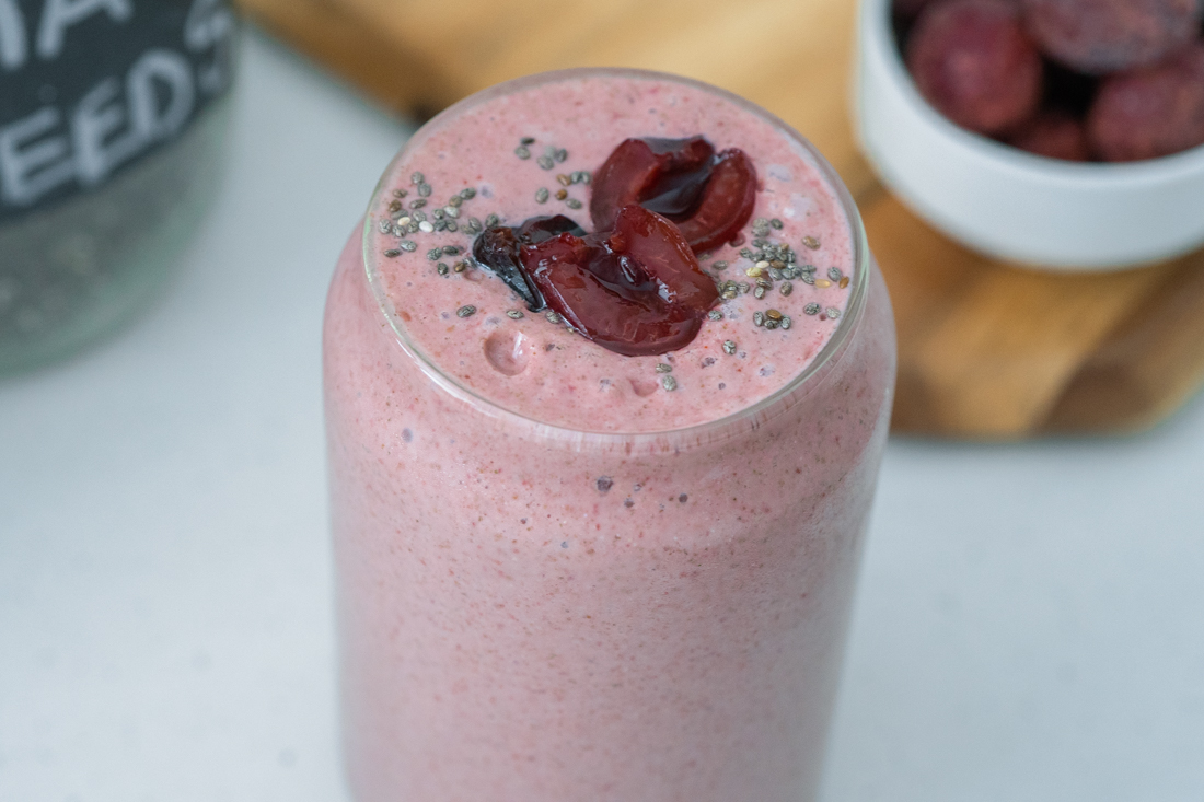 Cherry bomb smoothie in a glass cup. Topped with halved cherries and sprinkled with chia seeds.
