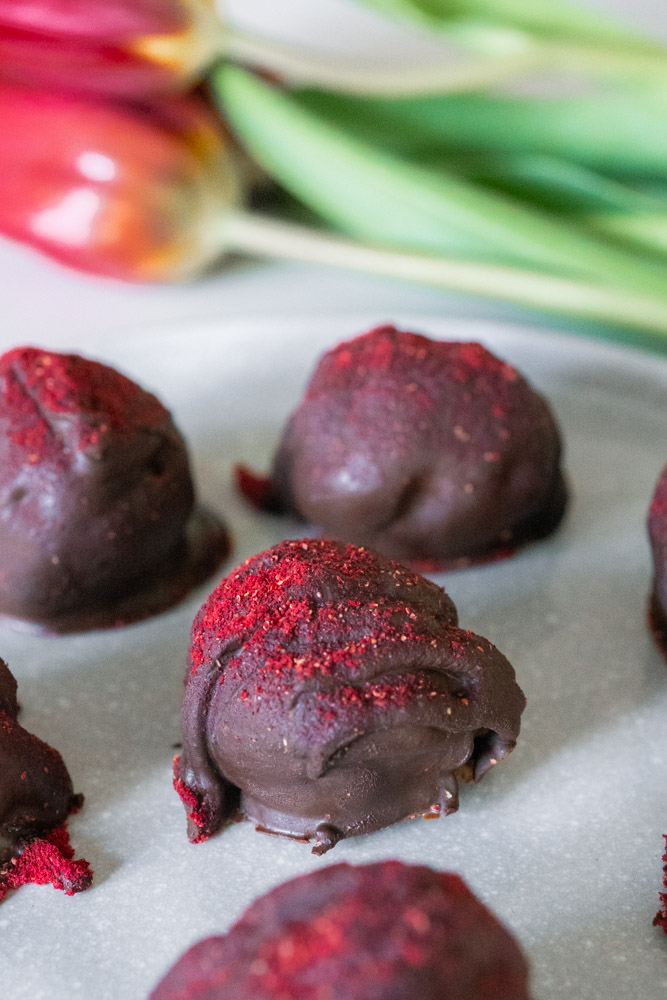 Double chocolate raspberry truffles on a light grey plate with red tulips in the background.