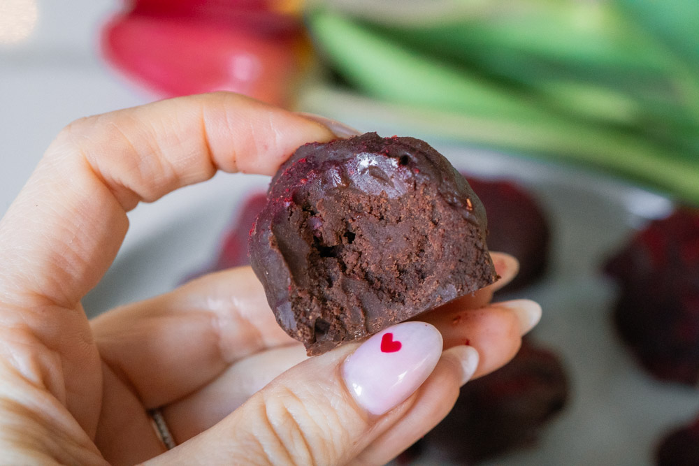 Double chocolate raspberry truffles being held with a heart on the woman's nail.