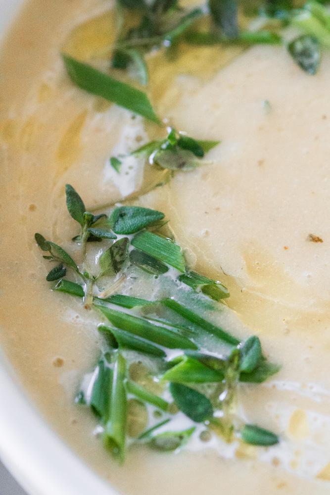 Roasted garlic potato leek soup in a white bowl. Up close of the fresh herb.
