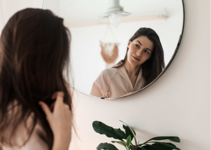 Acne impacts mental health in woman looking in the mirror hopeful.
