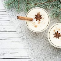 Homemade eggnog in glasses with star anise and cinnamon stick.