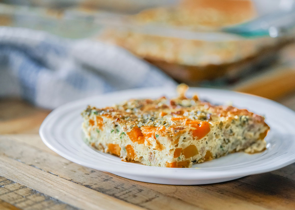 Overnight breakfast casserole with eggs, sweet potato, sausage, and fresh herbs on a white plate.