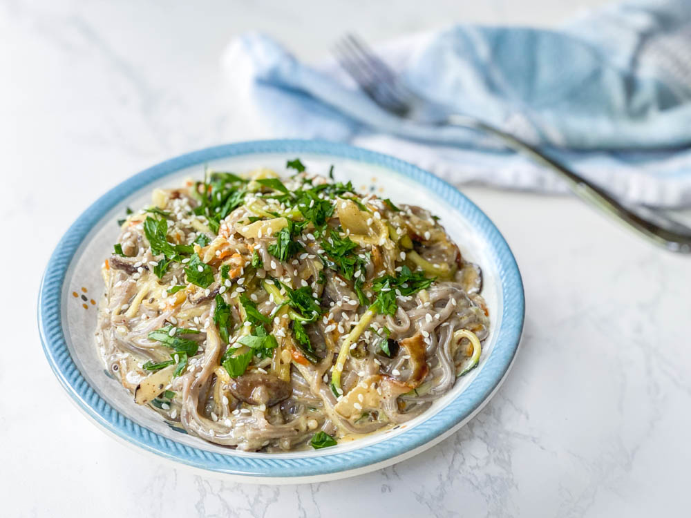 Soba noodle stir fry with creamy ginger sauce in a bowl on a white table.