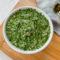 Kale & basil pesto in a small white bowl on wooden cutting board.