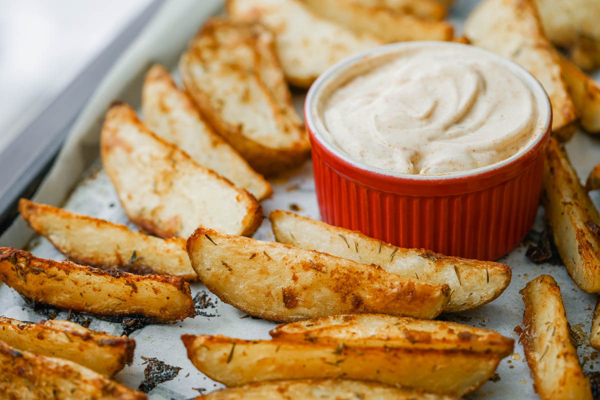 Crispy potato wedges on a baking sheet with honey dijon aioli.