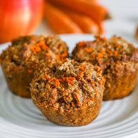 Grain-free and paleo morning glory muffins on a white plate with apples and carrots in the background.