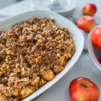Maple walnut apple crisp in a white casserole dish with apples on the table.