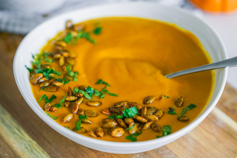 White bowl with pumpkin soup topped with fresh parsley and spiced pepitas.