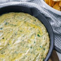 Hot spinach artichoke dip that's dairy free and shown in a cast iron pan with chips to the side.