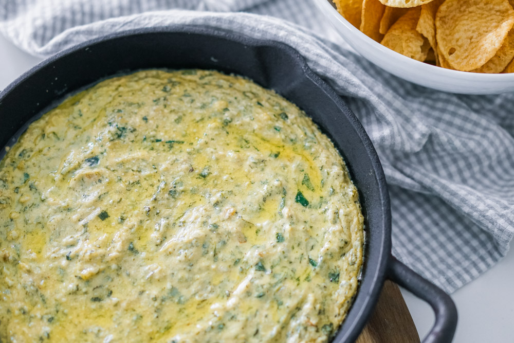 Hot spinach artichoke dip that's dairy free and shown in a cast iron pan with chips to the side.