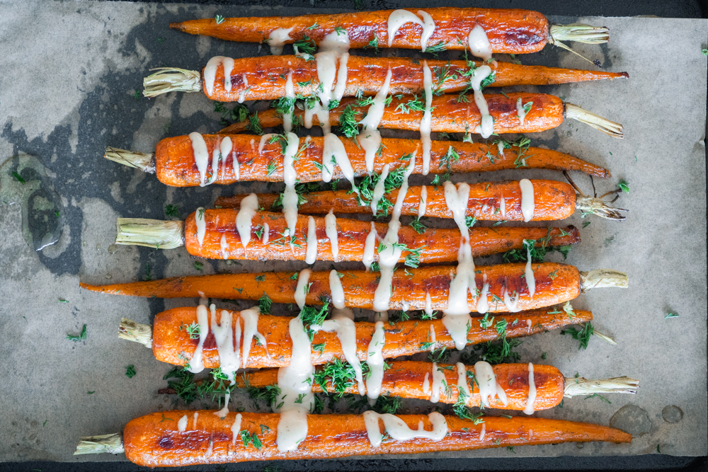 Honey dill carrots on a parchment paper lined baking sheet drizzled with roasted garlic aioli and sprinkled with fresh dill.