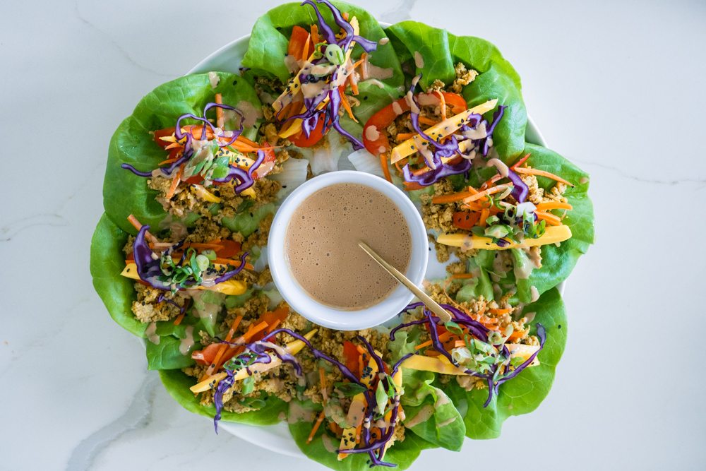 Rainbow lettuce wraps on a white platter with cashew butter sauce.