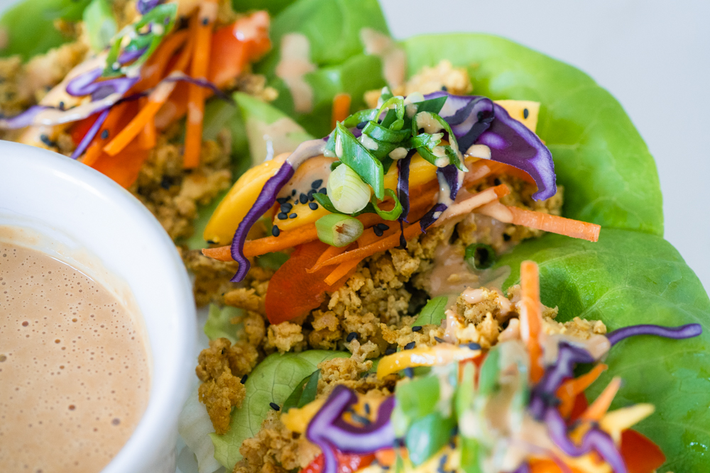 Rainbow lettuce wraps on a white platter with cashew butter sauce.