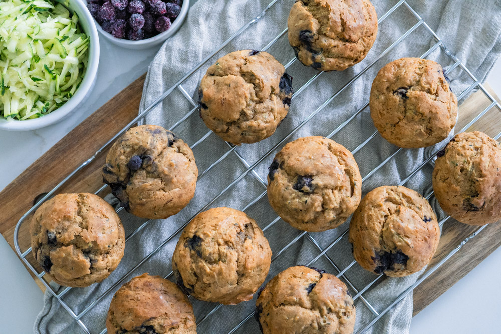 Blueberry Zucchini Muffins on a cooling rack with grey towel.