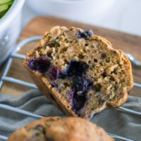 Blueberry Zucchini Muffins on a cooling rack with grey towel.