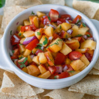 Peach salsa with fresh mint in a white bowl with tortilla chips.
