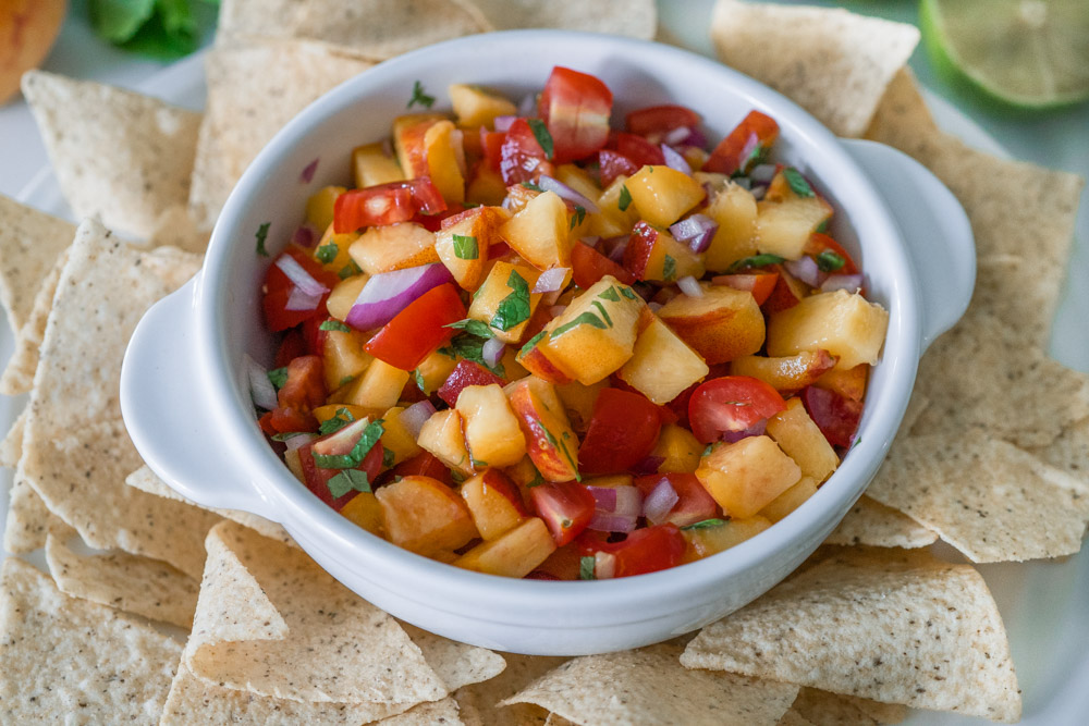 Peach salsa with fresh mint in a white bowl with tortilla chips.