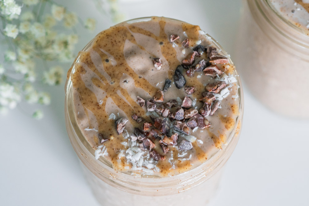 Cacao almond butter smoothie in a mason jar with cacao nibs and coconut sprinkled on top.