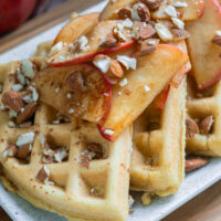 Gluten-free apple cinnamon waffles on a white plate with cooked apples on top.