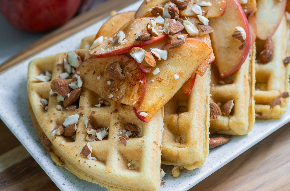 Gluten-free apple cinnamon waffles on a white plate with cooked apples on top.