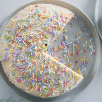 Gluten-free vanilla birthday cake on a plate with naturally dyed sprinkles.