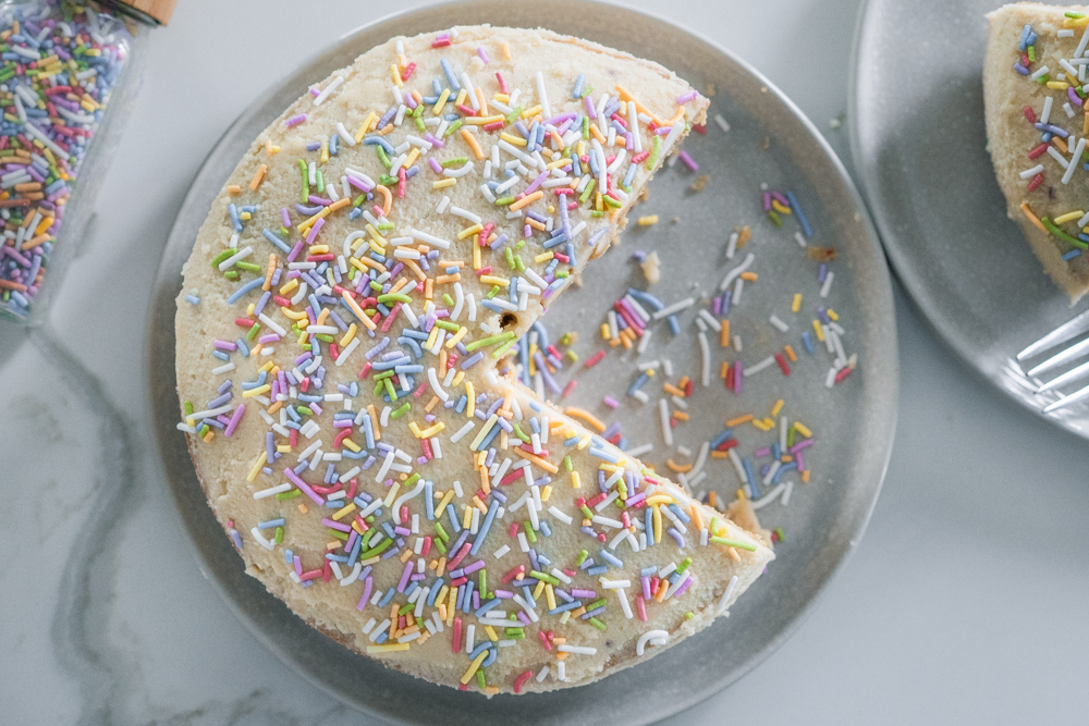 Gluten-free vanilla birthday cake on a plate with naturally dyed sprinkles.